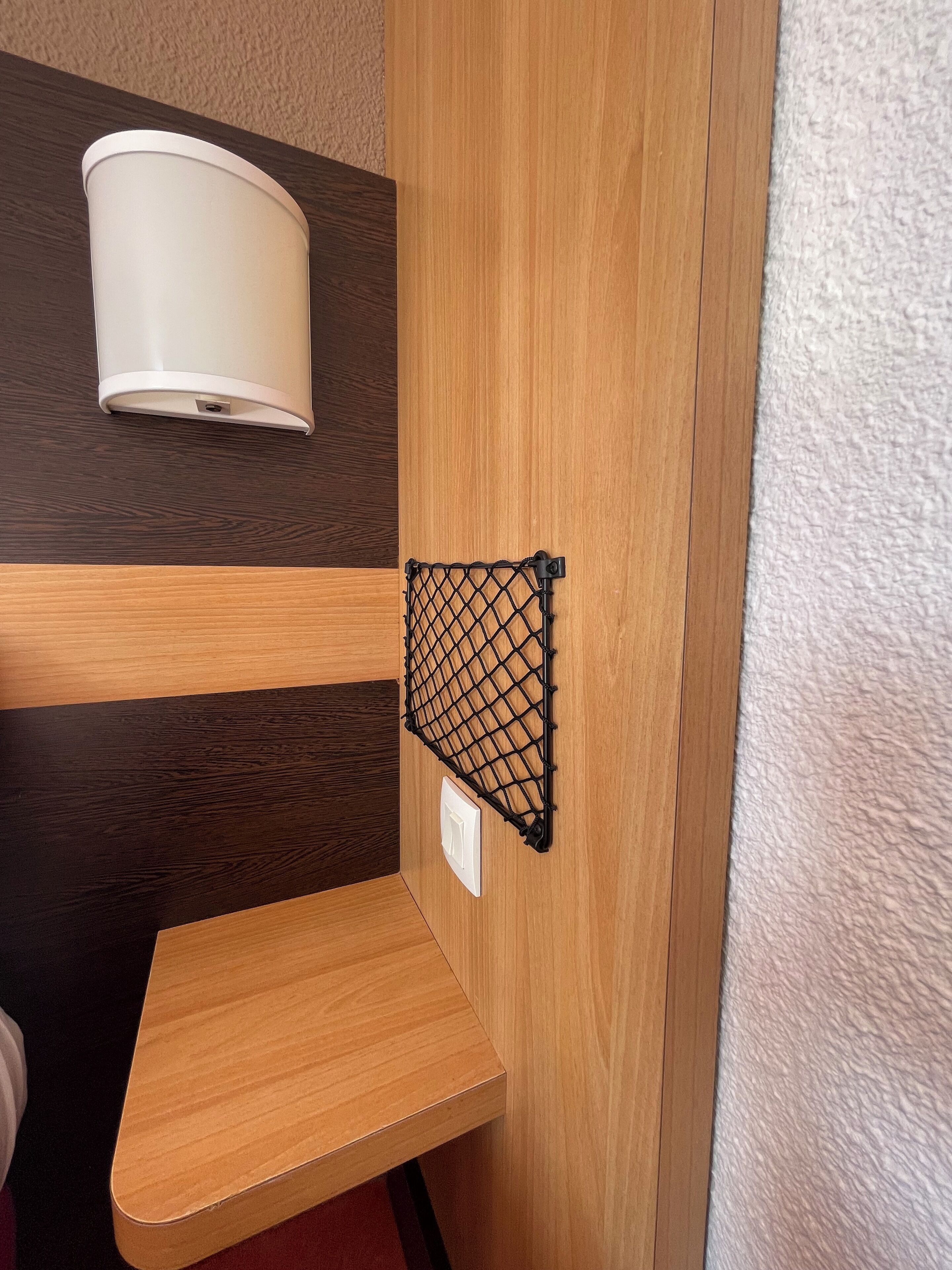 Een hoek van een kamer met een houten bankje, een wandlamp en een zwart metalen plank.