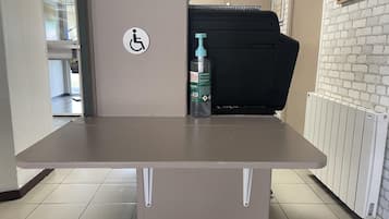 A table with a water bottle and a black printer in a room with a white brick wall and a door with a wheelchair accessibility sign.