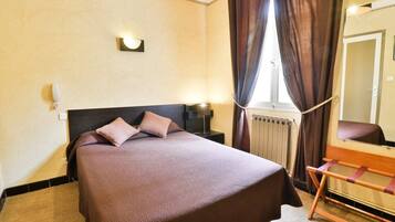 Una habitación de hotel con una cama grande, una mesita de noche con lámpara, un espejo y una ventana con cortinas.