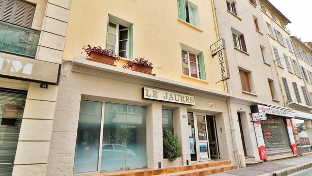 Un hotel llamado "LE JAURES" con fachada, ventanas amplias y un cartel que indica que es un hotel.