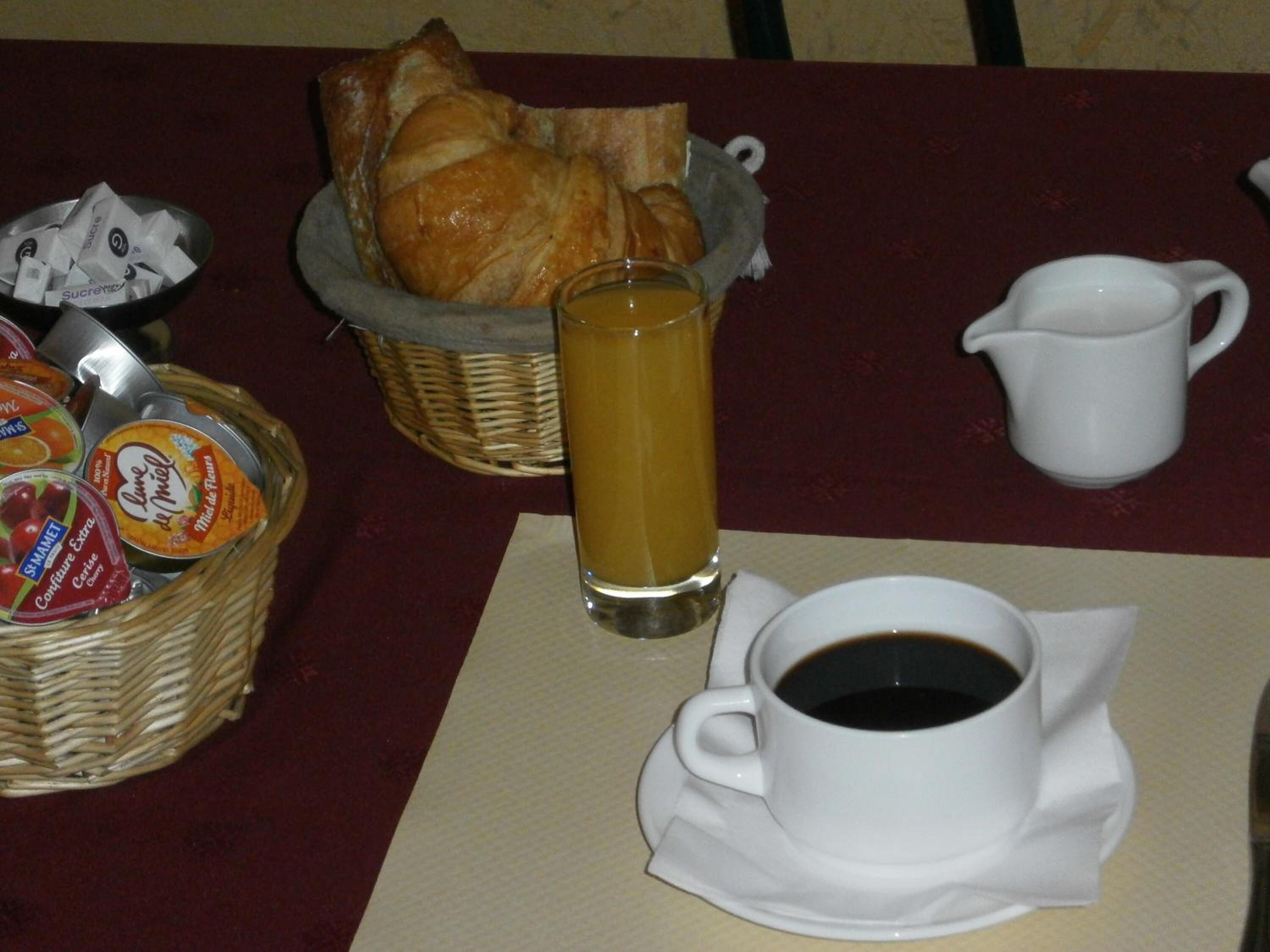 Ein Frühstückstisch mit Croissants, einem Glas Orangensaft, einer Tasse Kaffee und einer Auswahl an Marmeladen und Aufstrichen.