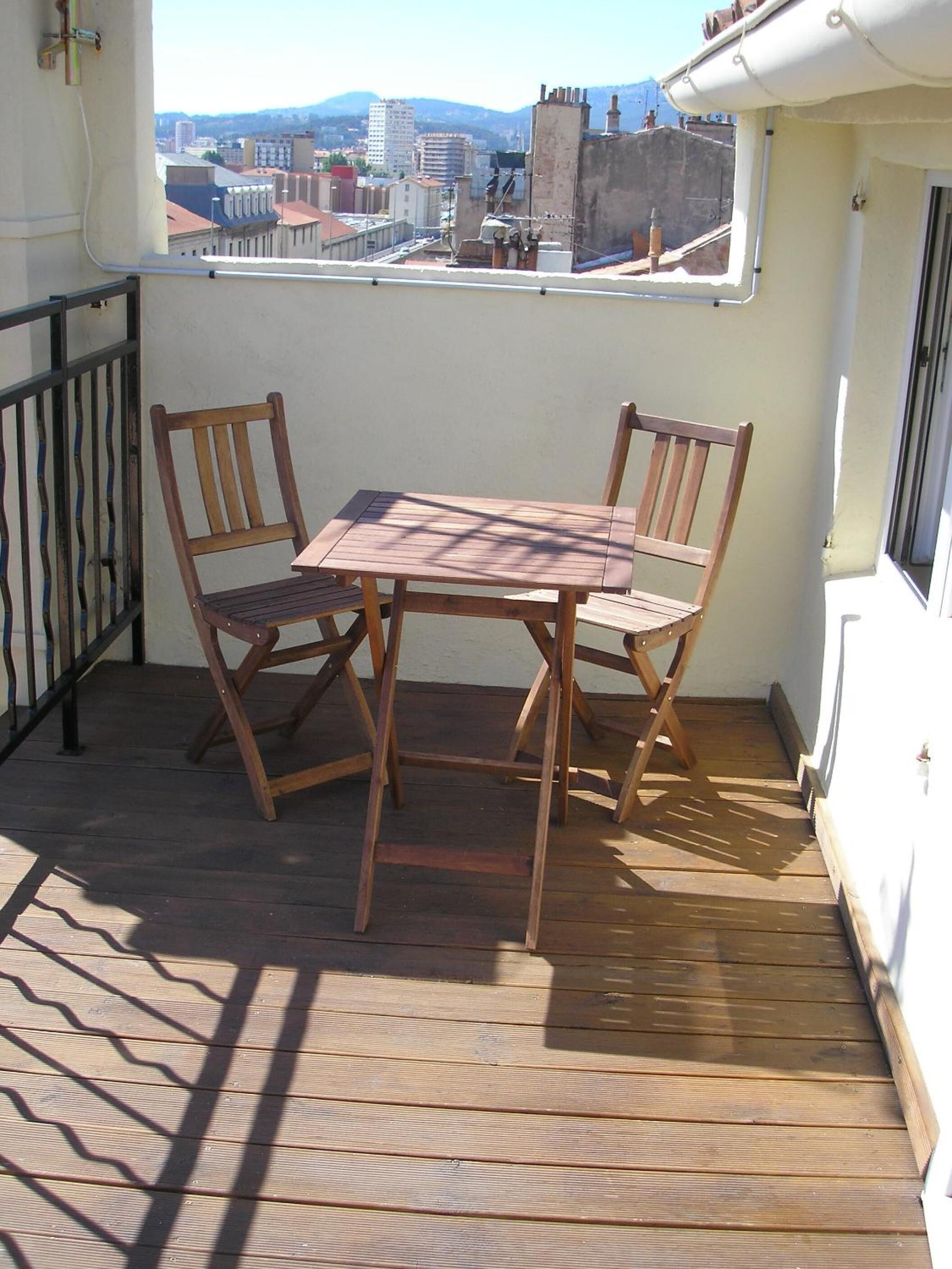 Een houten terras met een tafel en stoelen, met uitzicht op een stadsbeeld.