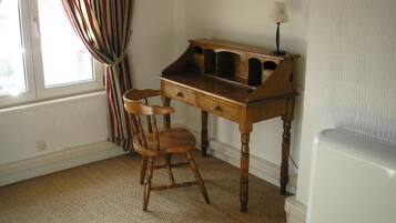 Une pièce avec un bureau en bois, une chaise, une lampe et un radiateur.