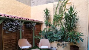 Un pequeño patio con dos sillas de mimbre, una valla de madera y varias plantas en macetas.