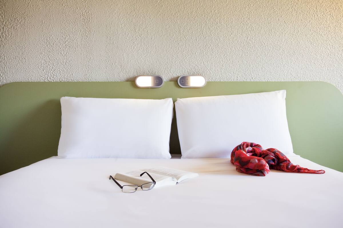 Un lit avec des oreillers blancs, une couverture à motifs rouges et noirs, et une paire de lunettes posée sur le lit.
