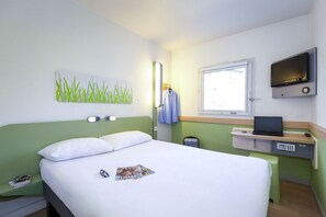 Een hotelkamer met een bed, een bureau met een laptop, een televisie en een raam.