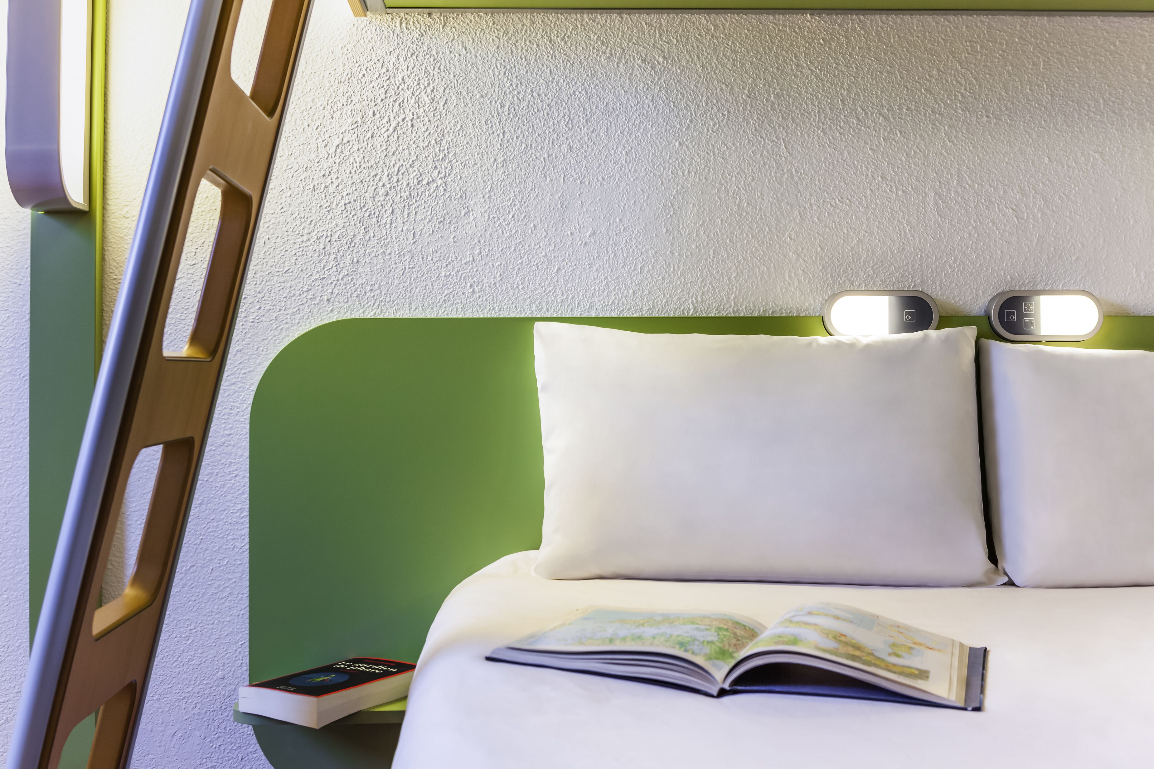Un lit avec une tête de lit verte, deux lampes de chevet et un livre ouvert posé sur le lit.