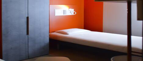 A small, compact room with a bed, a wardrobe, and a desk.