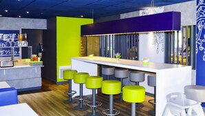 Un espace bar moderne avec un comptoir blanc, des tabourets verts et un mur d’accent violet.