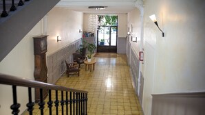 Un pasillo con una escalera de madera, una mesa redonda con sillas y una planta en maceta.
