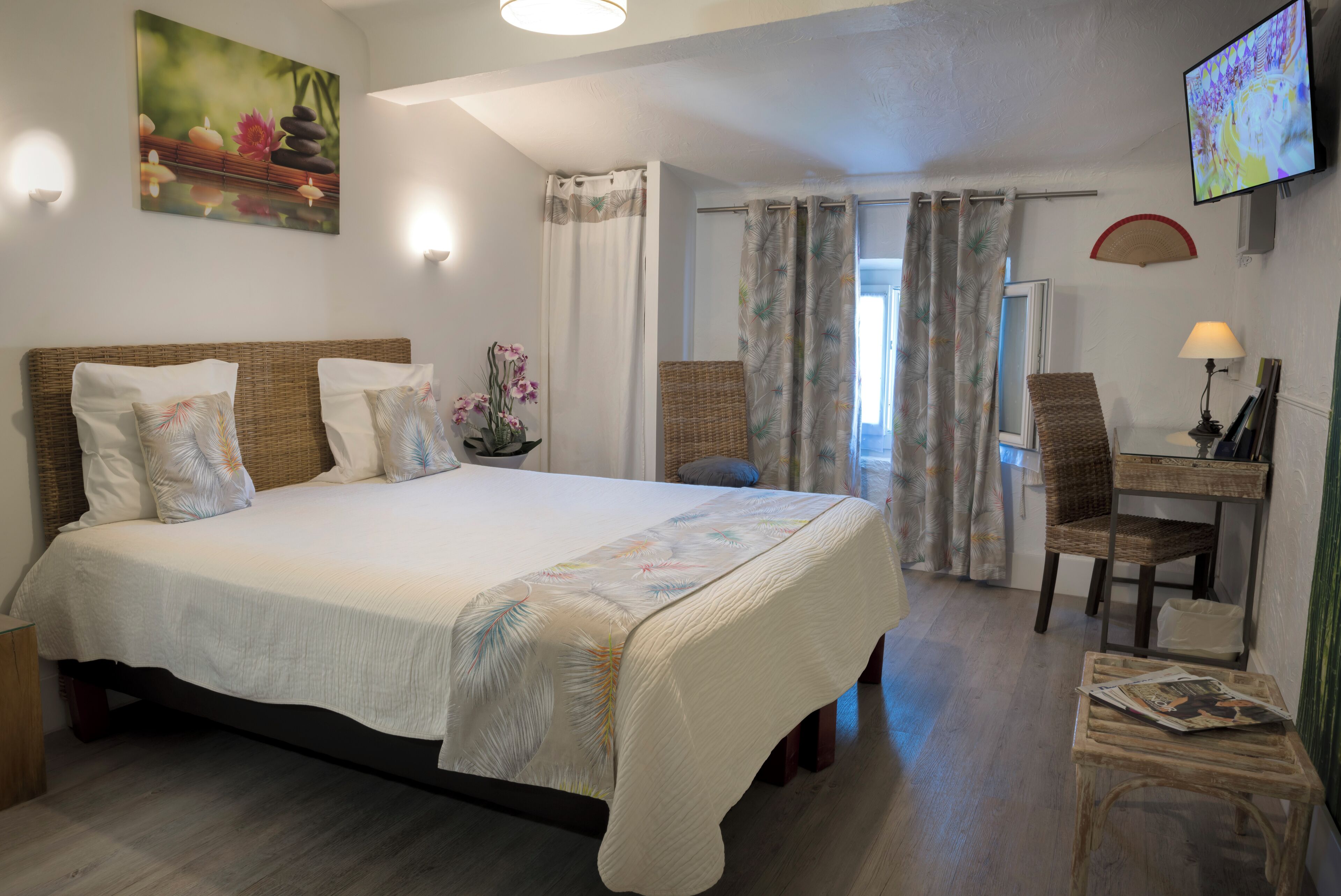 Ein Schlafzimmer mit einem Bett, einem Schreibtisch, einem Sessel, einem Fernseher und einem Fenster mit Vorhängen.