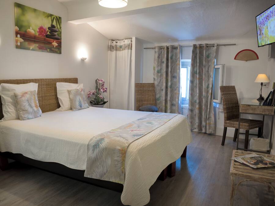 Ein Schlafzimmer mit einem Bett, einem Schreibtisch, einem Sessel, einem Fernseher und einem Fenster mit Vorhängen.