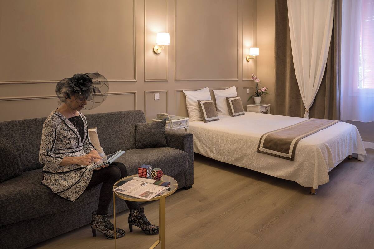 A hotel room with a bed, a sofa, a small table with a lamp, and a nightstand.
