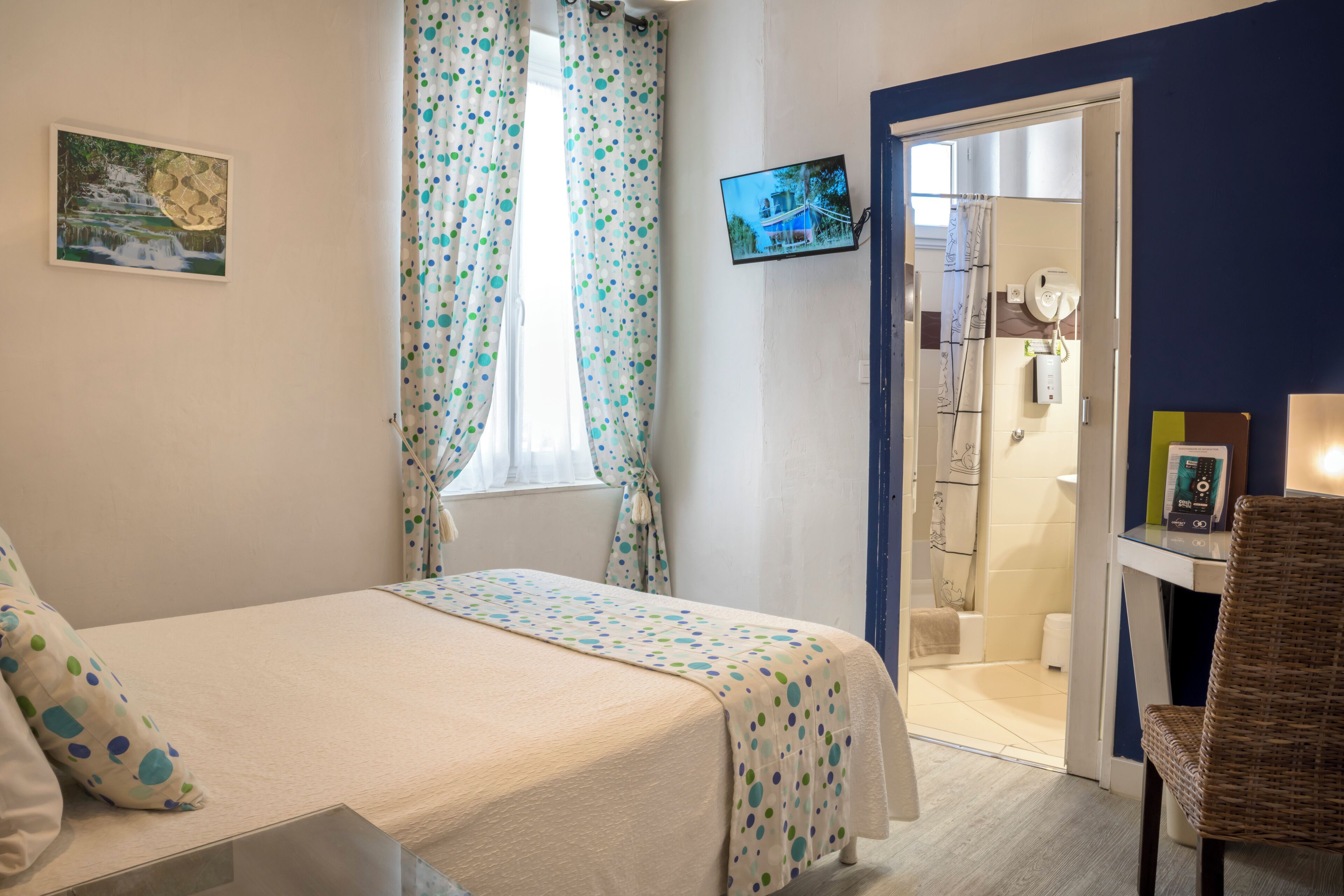Un dormitorio con cama, televisión, baño con ducha y una silla.