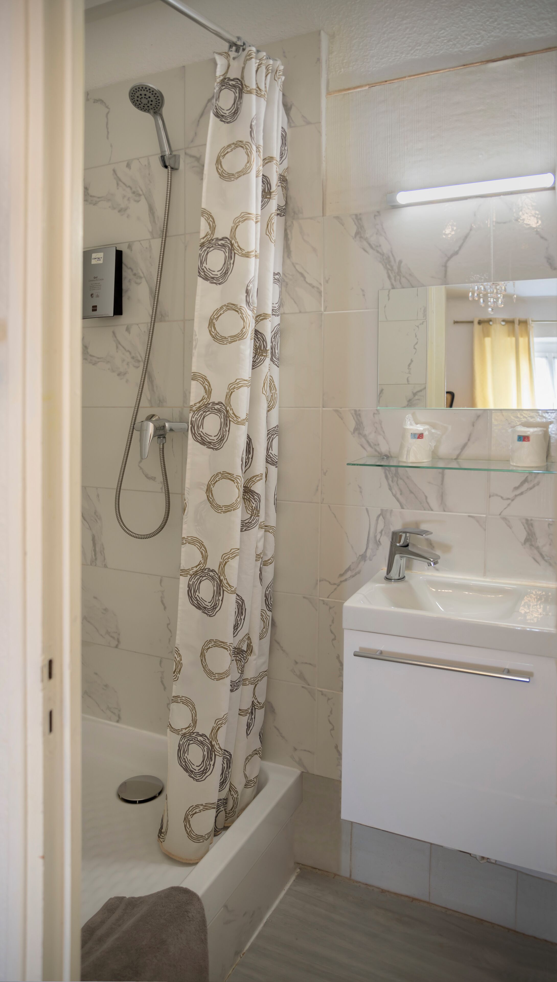 A bathroom with a shower, a bathtub, a glass shelf with toiletries, and a sink.