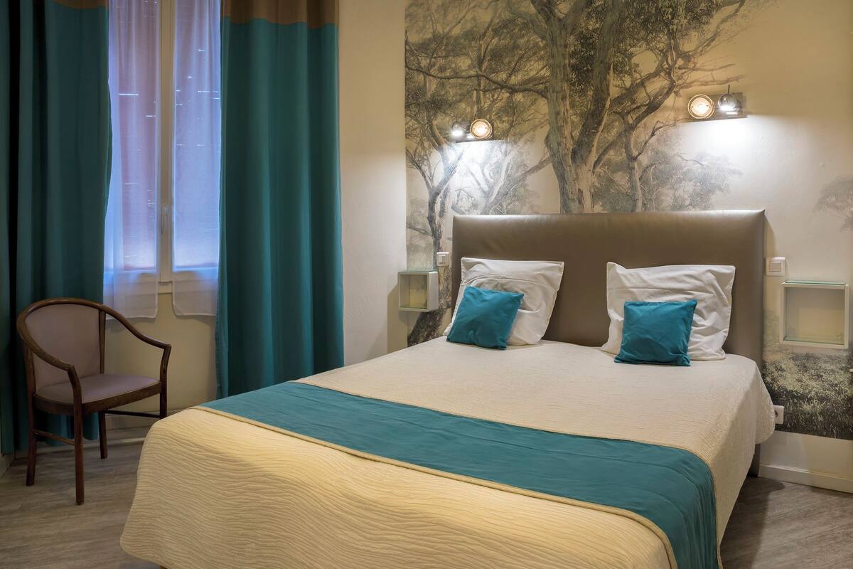A hotel room with a bed, a chair, and a wall mural.