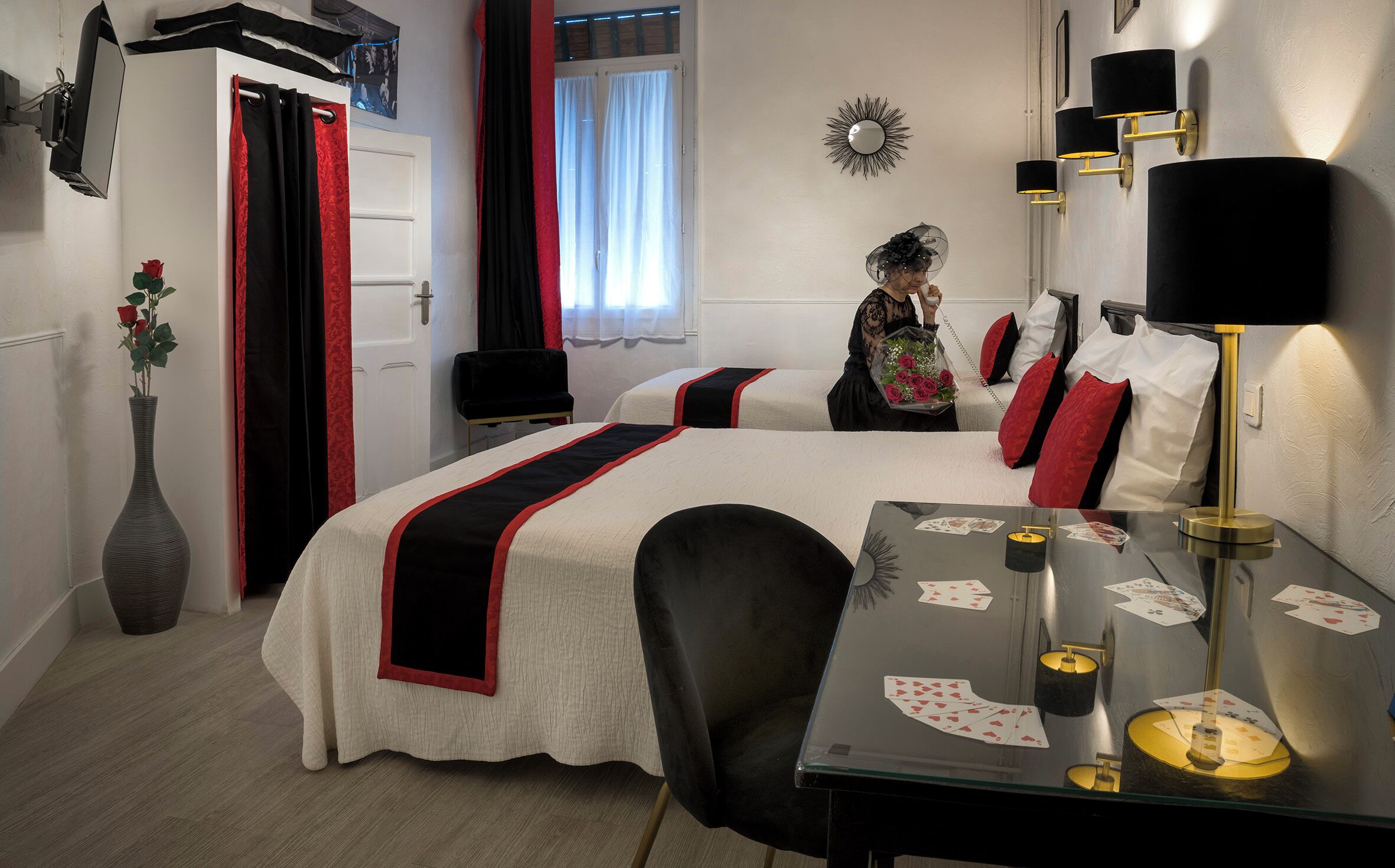 Una camera d'albergo con un letto, comodini, una scrivania e una sedia. Sul pavimento, un vaso con un fiore.
