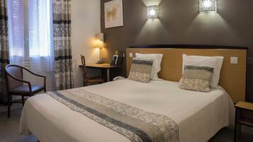 A neatly made bed with a headboard, a bedside table with a lamp, a chair, and a window with curtains.