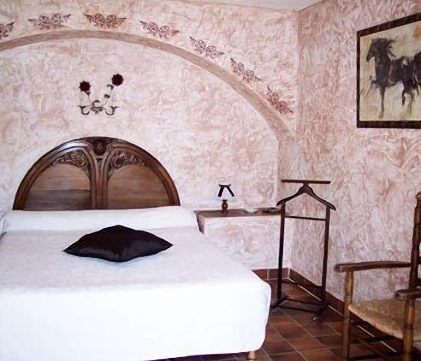 Ein Schlafzimmer mit einem großen Bett, einem hölzernen Kopfteil, einem Nachttisch, einem Sessel und einer Wandleuchte.