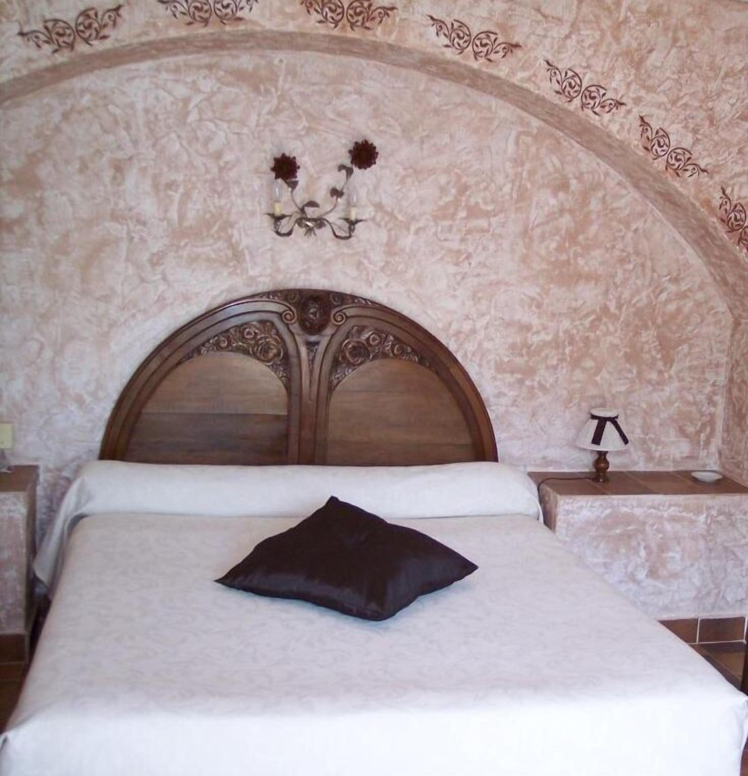 Un dormitorio con cabecera de madera, una almohada negra individual, una lámpara de noche y un aplique en la pared.