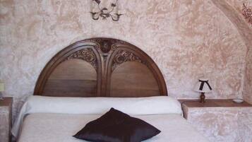 A bedroom with a wooden headboard, a single black pillow, a bedside lamp, and a wall-mounted light fixture.
