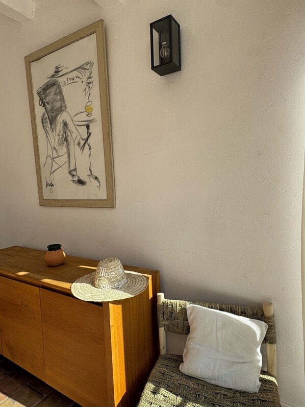 Una habitación con un aparador de madera, una cesta tejida, un sombrero de paja y una obra de arte enmarcada en la pared.