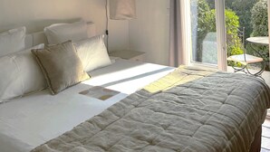 A bedroom with a large bed, a bedside table, a hanging lamp, and a view of the outdoors through a sliding glass door. - Le Mas de Garrigon - Boutique Hôtel & Spa (Roussillon)