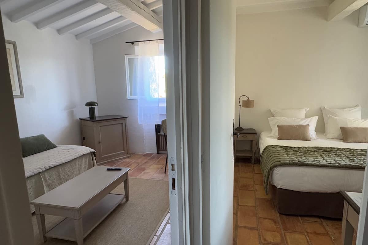 A bedroom with a bed, bedside table, lamp, and a view of a bathroom.