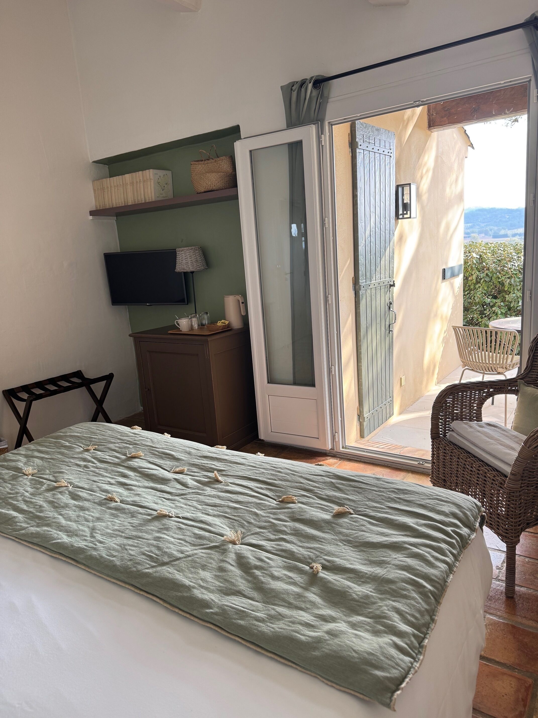 A bedroom with a bed, a TV, a desk, a chair, and a sliding glass door leading to a balcony.