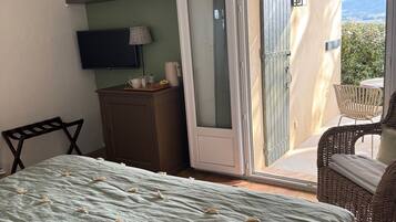 A bedroom with a bed, a TV, a desk, a chair, and a sliding glass door leading to a balcony.