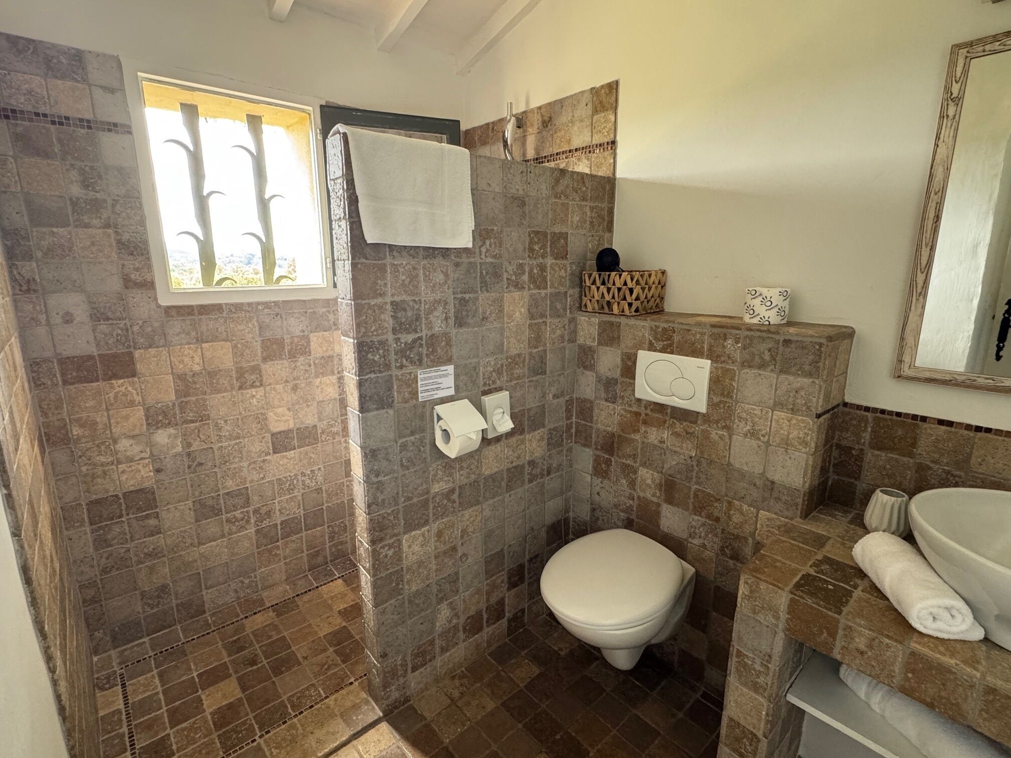 A bathroom with a shower, toilet, and sink, featuring stone tiles and a window.