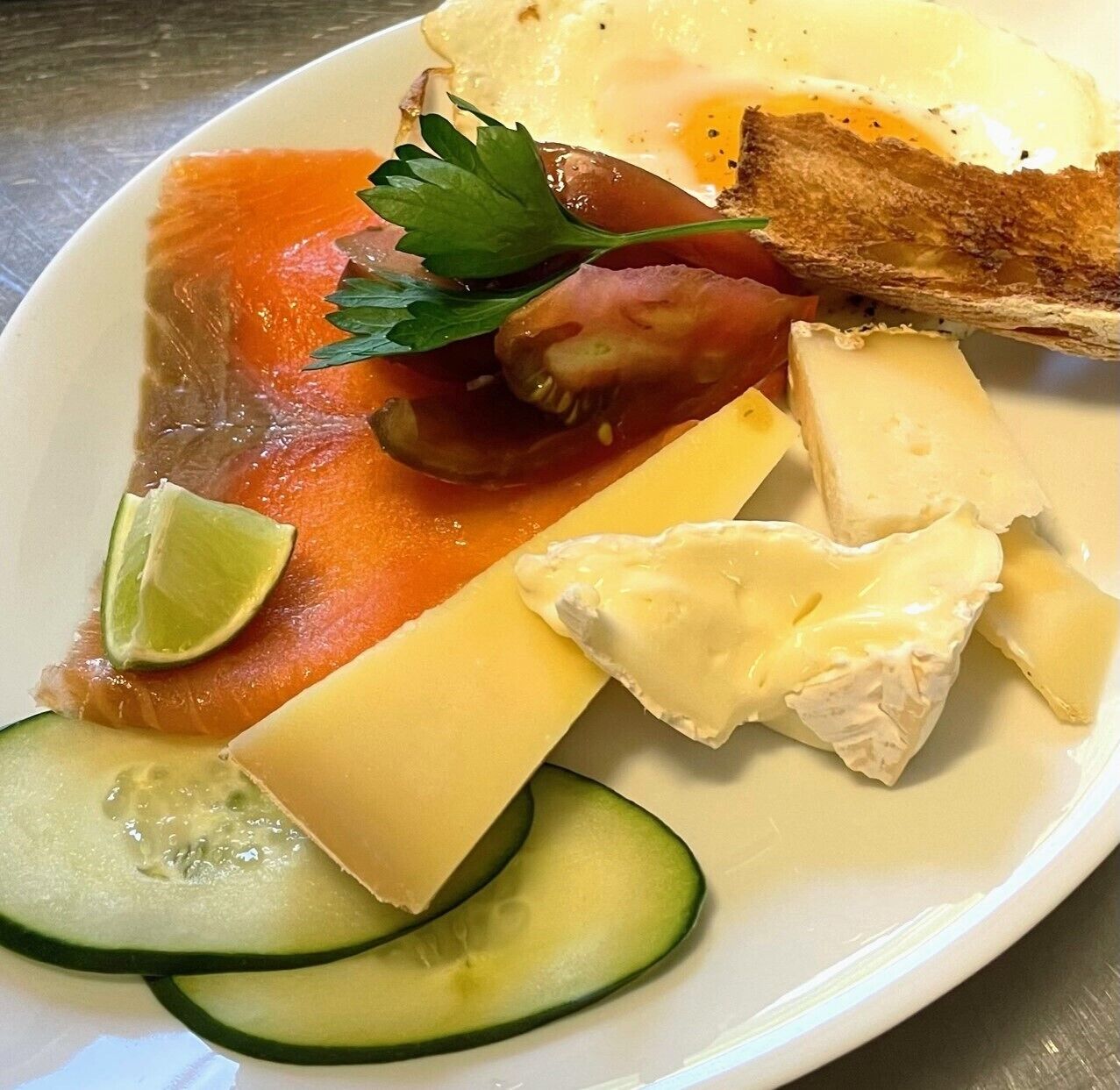 A plate with various food items including salmon, cheese, a fried egg, and cucumber slices.