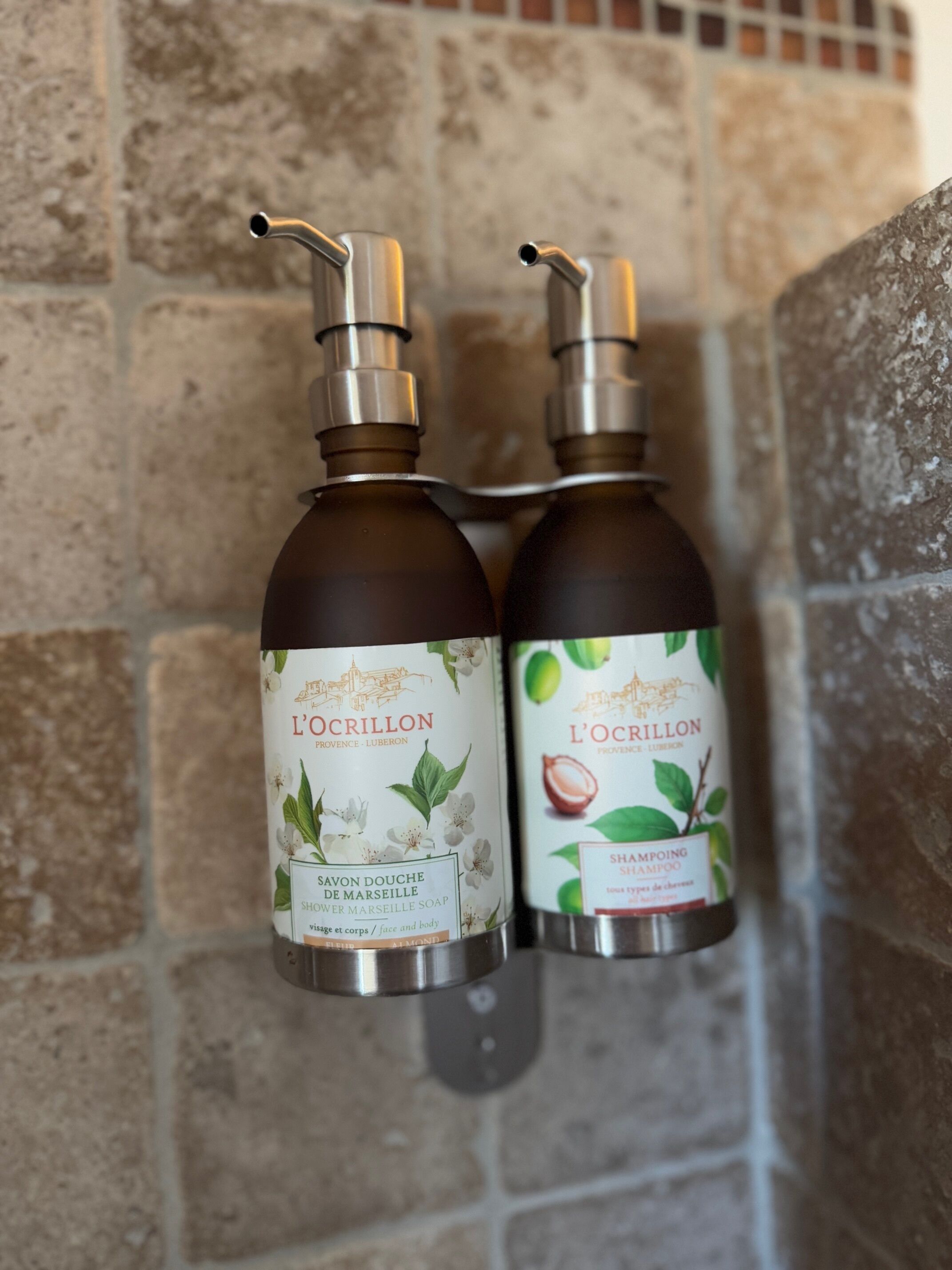 Due flaconi di shampoo e sapone L'Ocrillon fissati a una parete in pietra.