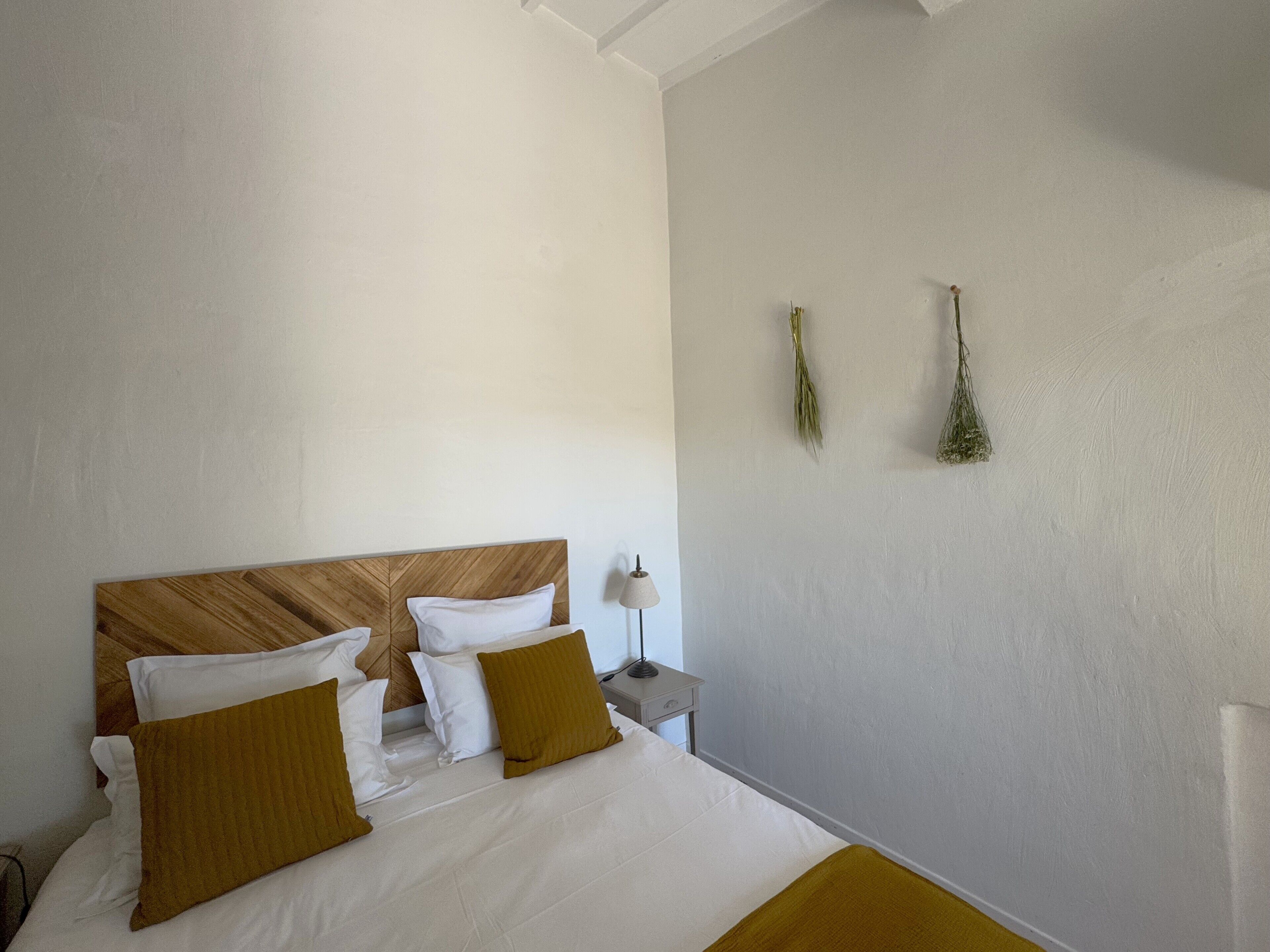 A neatly made bed with a wooden headboard, white and mustard-colored pillows, and a bedside table with a lamp.