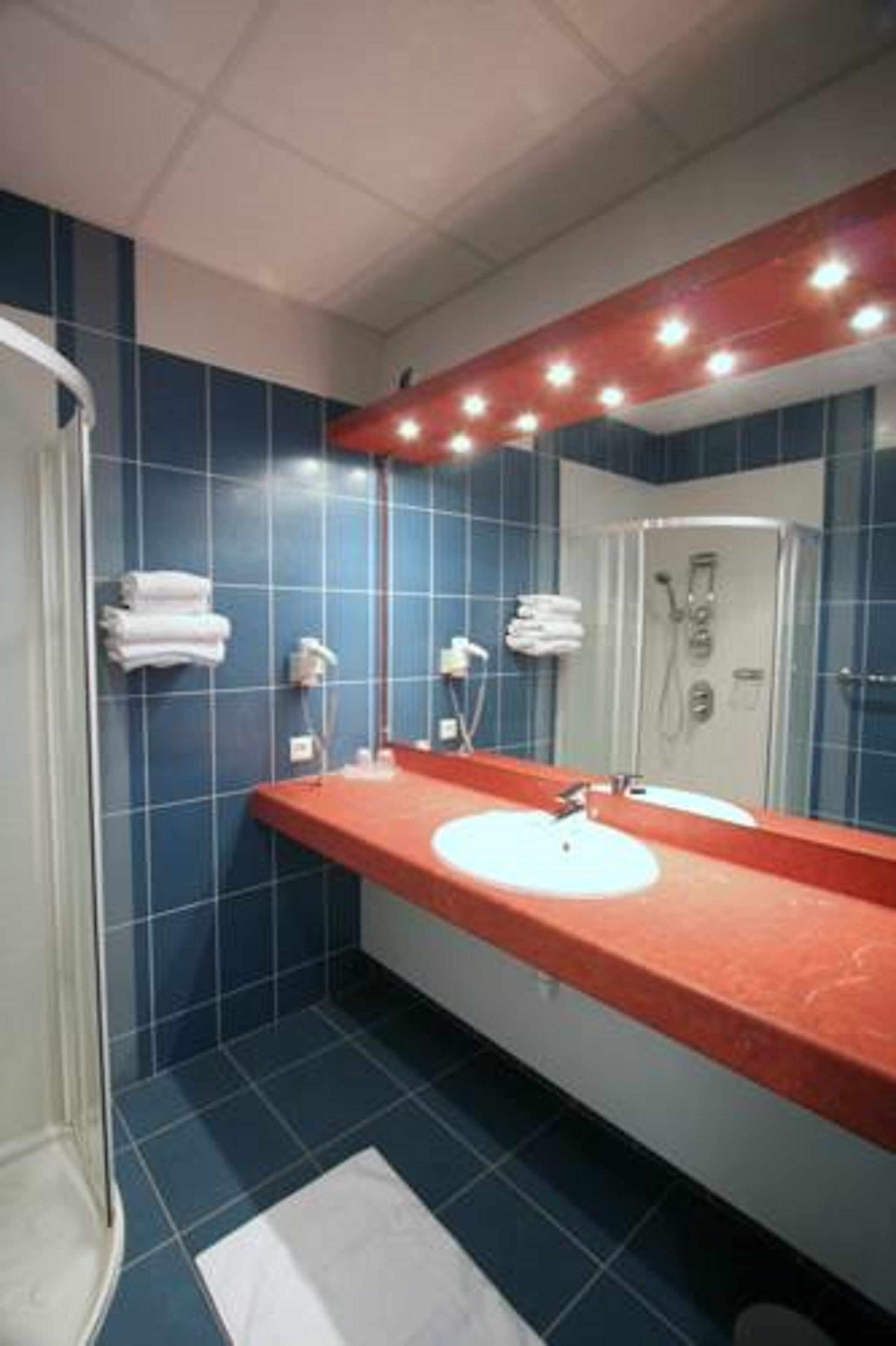 Een badkamer met blauwe tegels, een rode wastafel, een witte wasbak, een spiegel en een douchegedeelte.