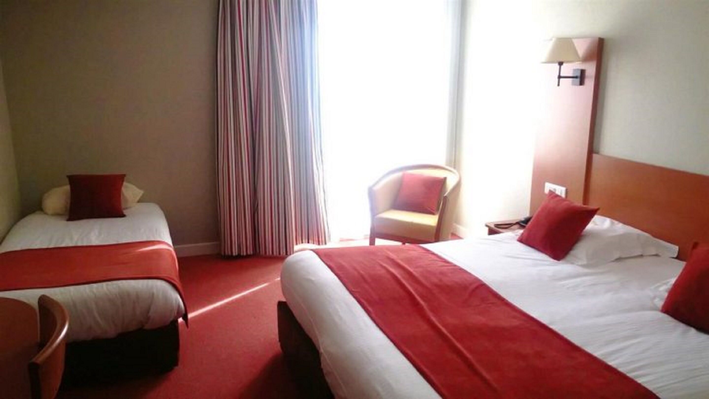 A hotel room with two beds, a chair, a lamp, and a window with curtains.