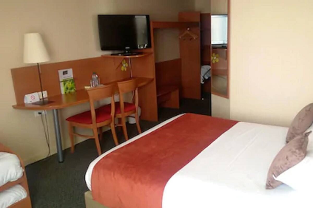 A hotel room with a bed, a desk with a chair, a television, and a wardrobe.