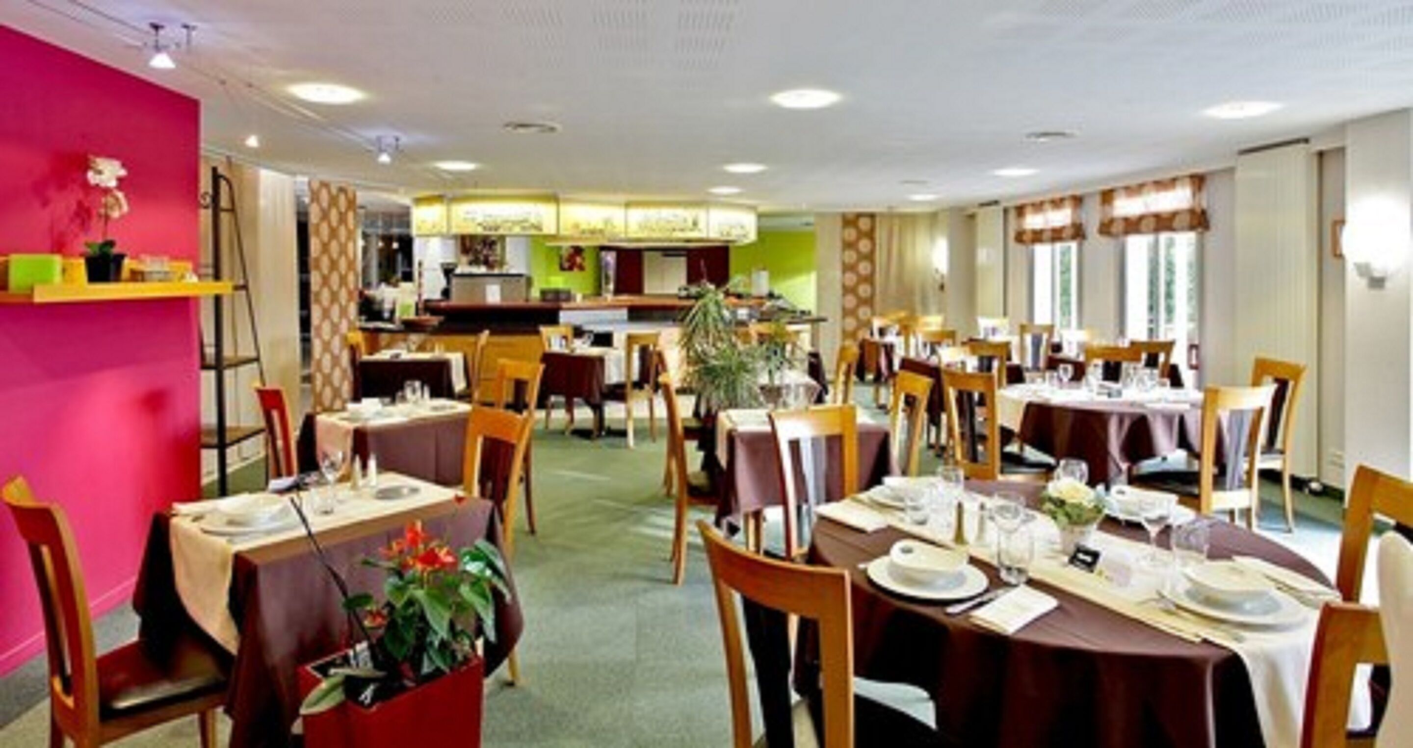 A restaurant with multiple tables set for dining, a counter area, and a visible kitchen in the background.