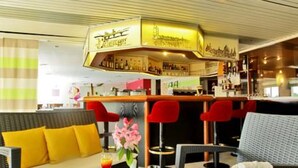 Una zona de bar con mostrador y taburetes, un sofá con cojines amarillos y una mesa de vidrio con una revista y bebidas.