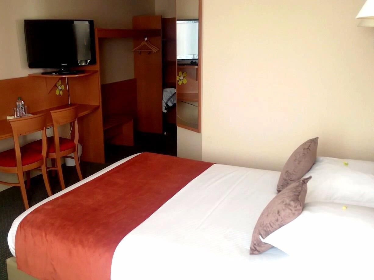 Une chambre d’hôtel comprenant un lit, une télévision, un bureau avec une chaise et une armoire.