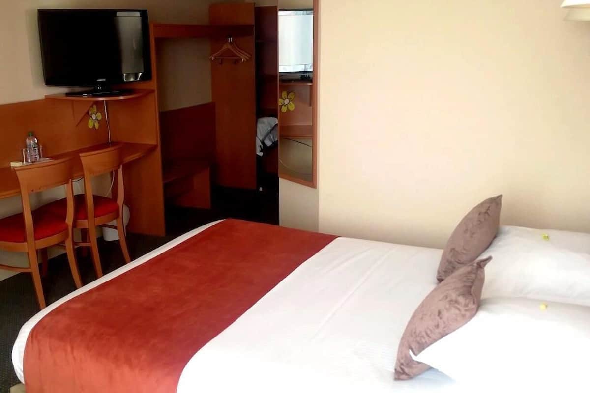 A hotel room with a bed, a TV, a desk with a chair, and a wardrobe.