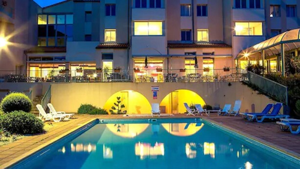 Un hotel con piscina, tumbonas y una zona cubierta con sombrillas.