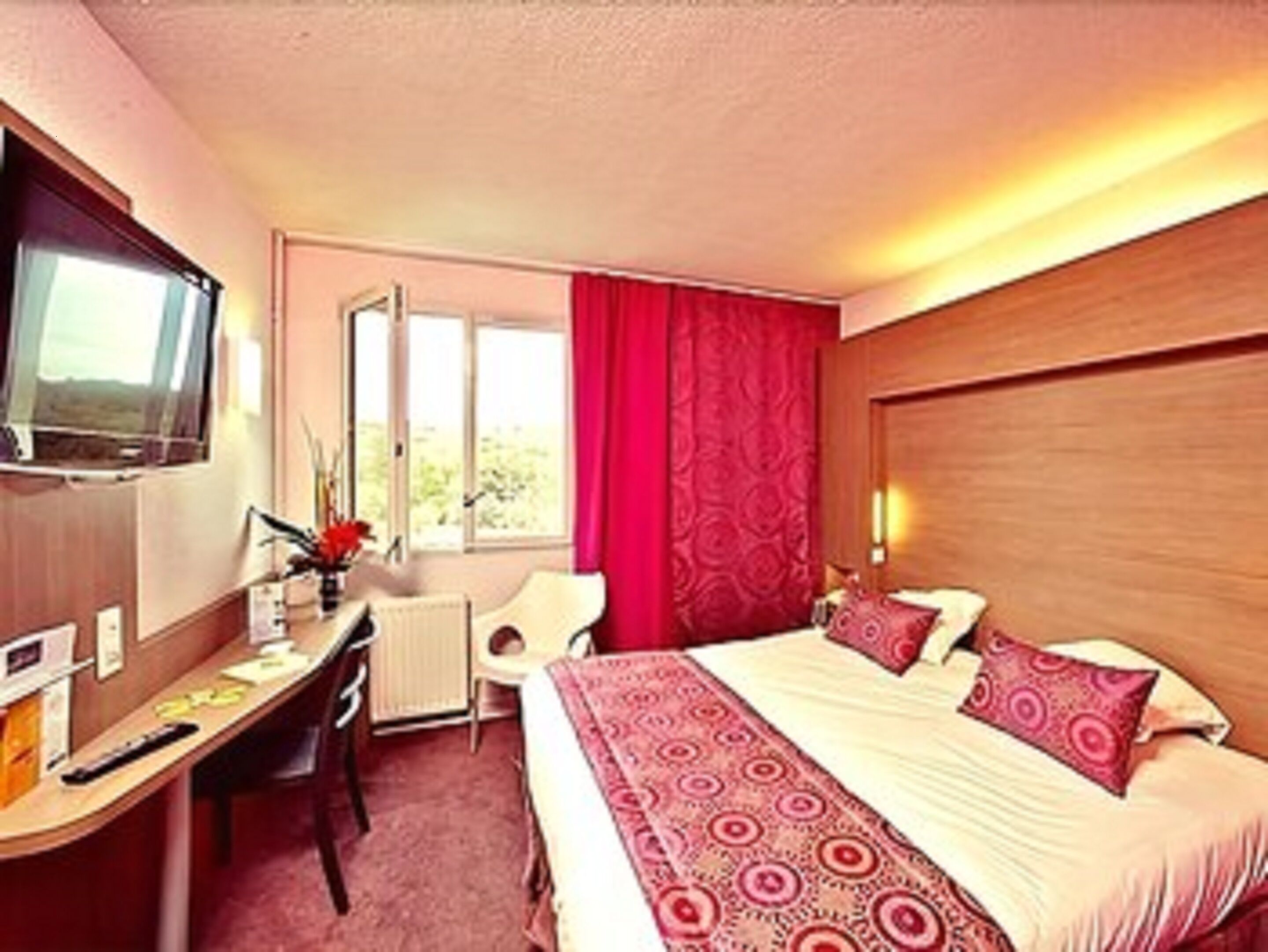 A hotel room with a bed, a desk, a chair, a TV, and a window with curtains.