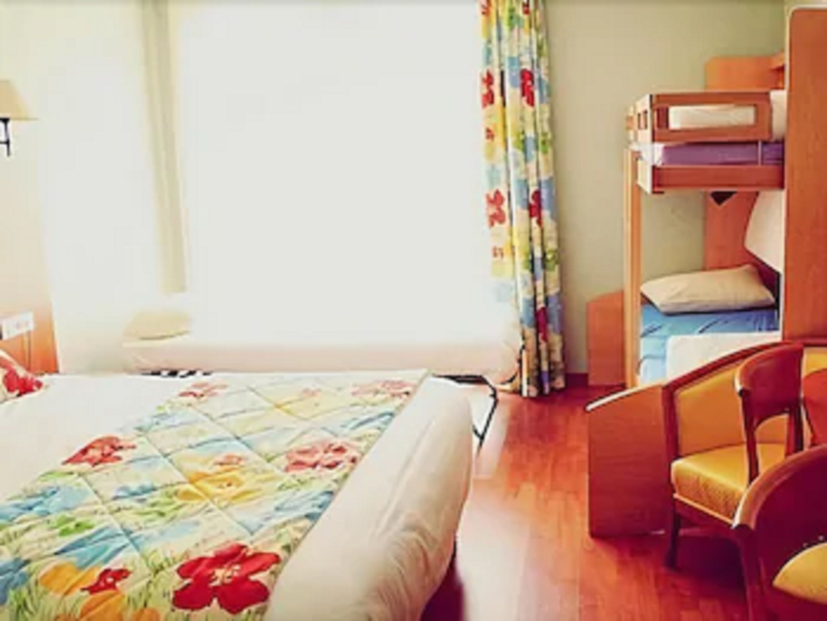 A hotel room with a bed, a chair, a desk, and a window with curtains.