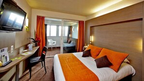 Habitación de hotel con cama, escritorio, silla, televisión y puerta corrediza a un balcón.