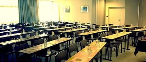 Un salón de conferencias con varias mesas y sillas, dispuestas en filas.