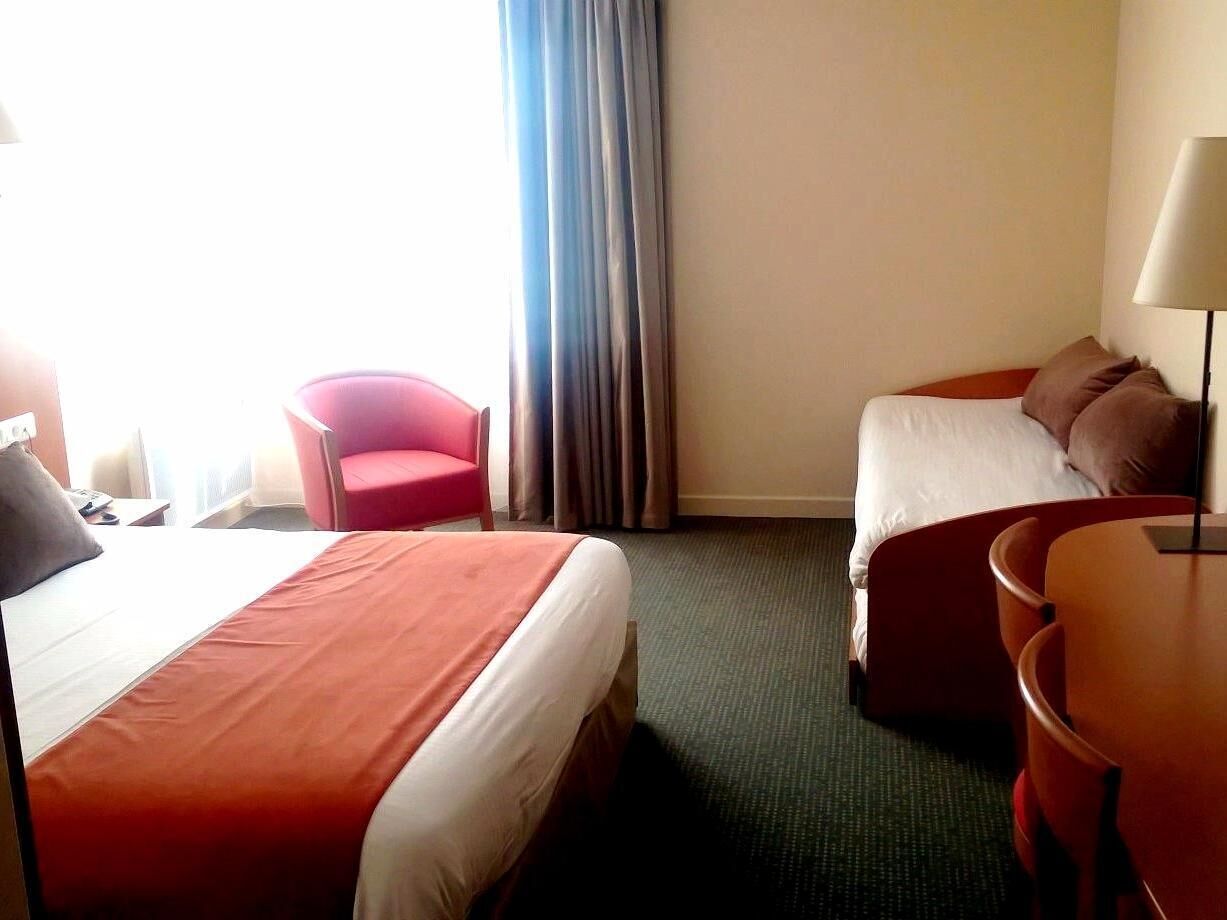 Une chambre d’hôtel avec deux lits, un bureau, une chaise et une lampe.