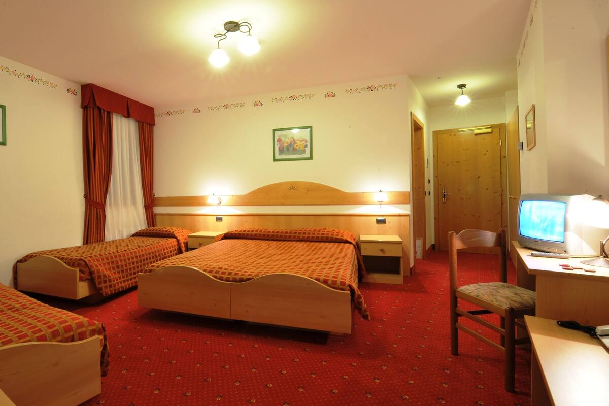 A hotel room with two single beds, a desk with a computer, a chair, and a television.