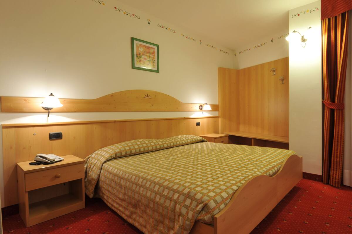 A hotel room with a wooden bed, two bedside tables, a nightstand, a wardrobe, and a window with curtains.