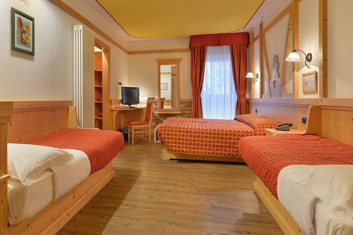 A hotel room with two single beds, a desk with a computer, a chair, and a large mirror.